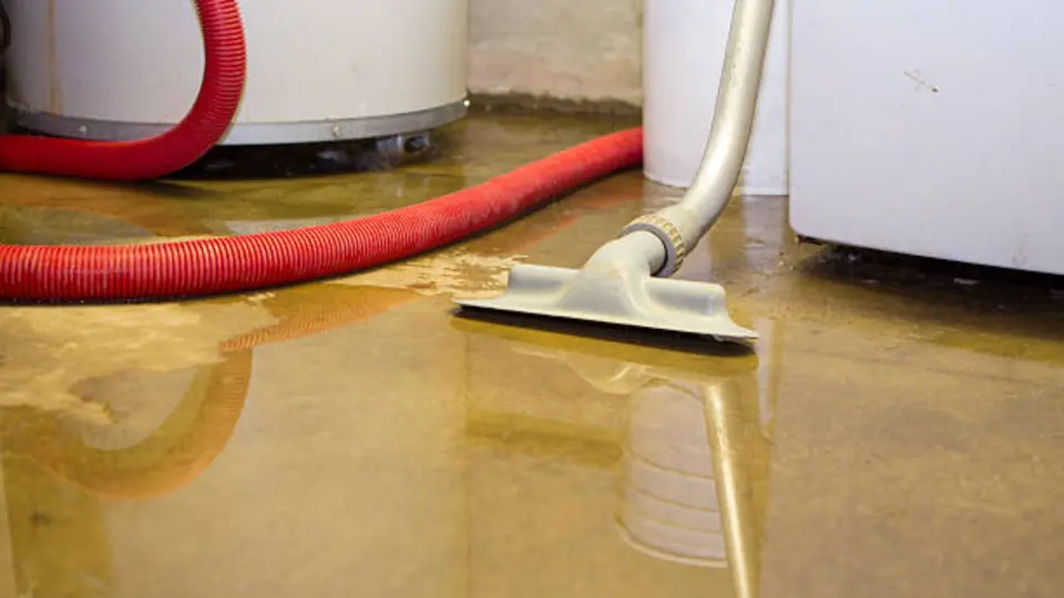 Wet vacuum nozzle pulling water off a floor beside a water heater