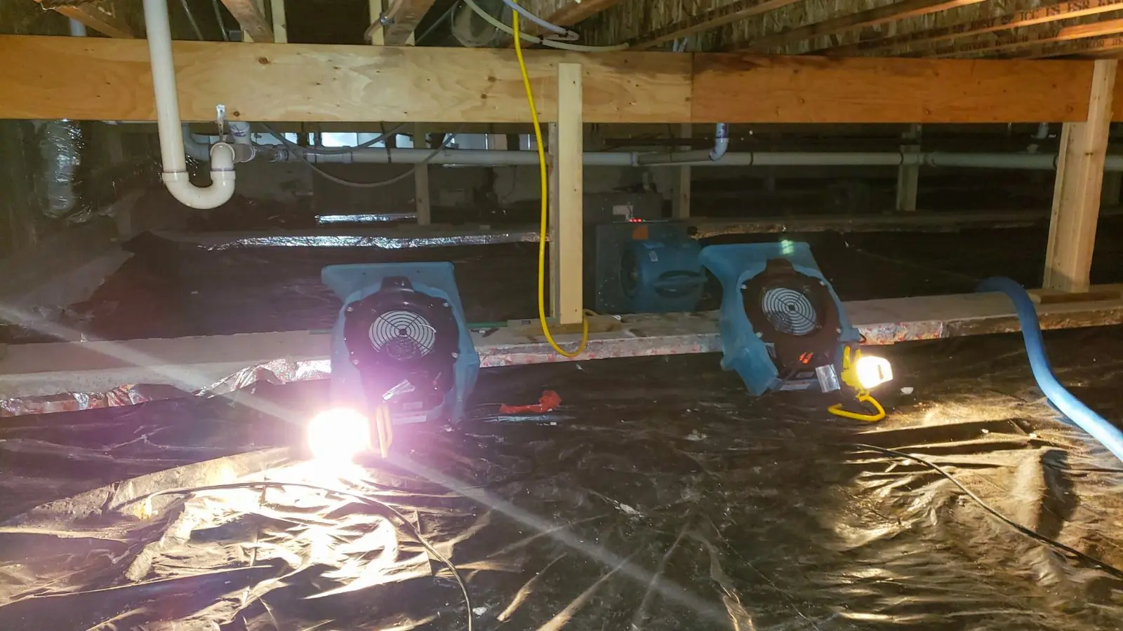 Air movers and work lights running over plastic sheeting in a crawl space