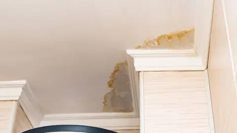 Brown water stain on a ceiling corner above trim