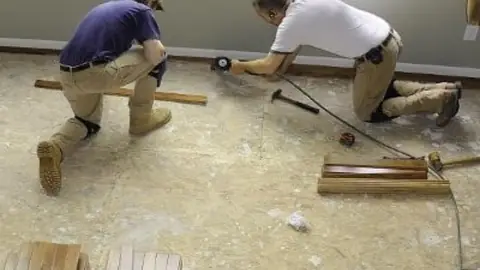 Two workers kneeling on a bare subfloor during a floor repair