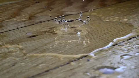 Water droplets splashing on wet wooden floor boards